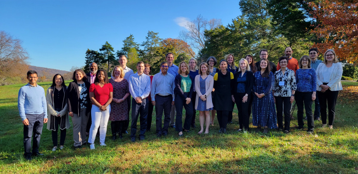 Group photo of LAM participants standing outside on a grassy hill with trees in the background. 